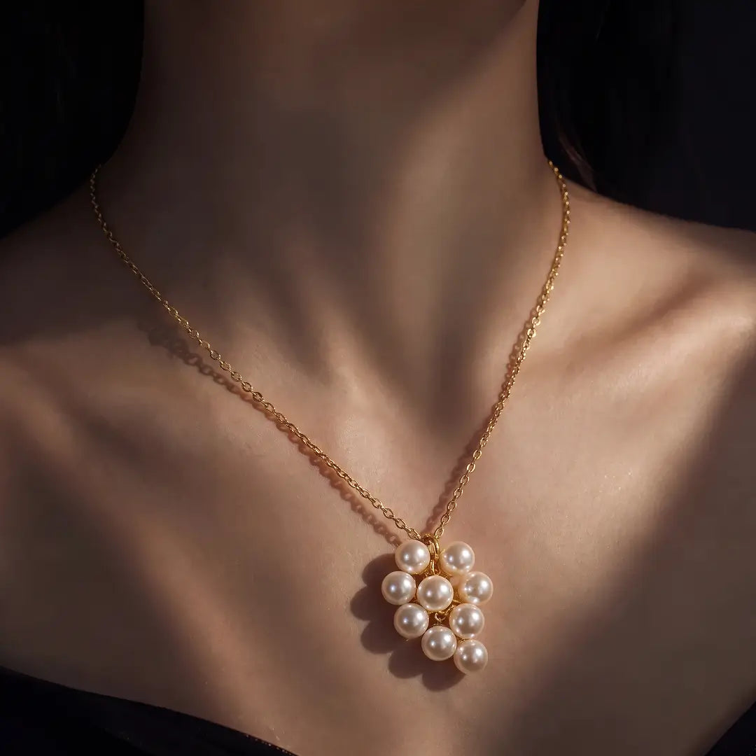 A gold chain necklace with a cluster of white faux pearls pendant, shown worn on a model's neck against a dark background.