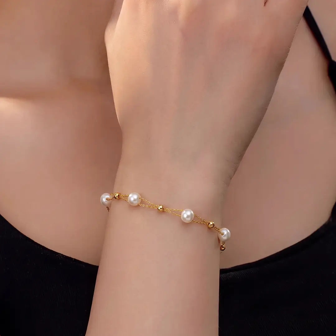 A delicate gold chain bracelet with small white pearls and gold beads, shown worn on a person's wrist.