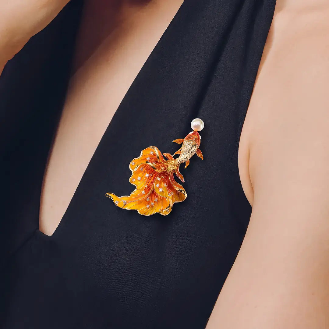 Aiko Tanaka Kasane brooch, an orange enamel goldfish with a white pearl, worn on a black sleeveless V-neck top