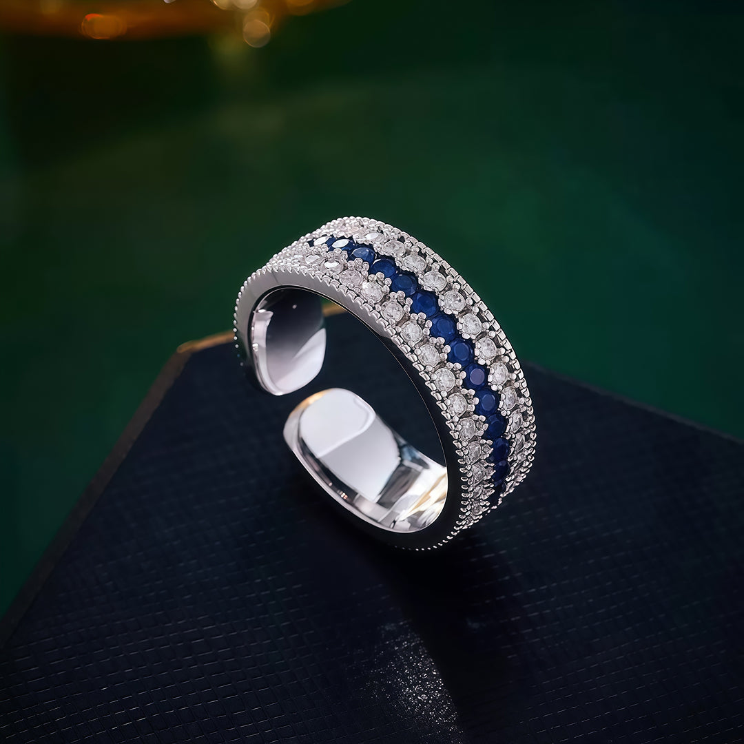 Aiko Tanaka Kiseki silver ring with rows of blue stones and white crystals on a dark stand before a green background