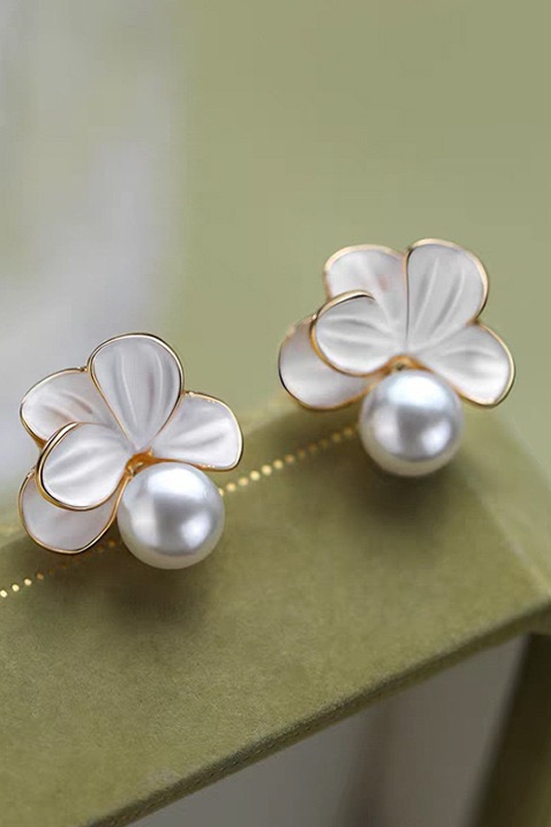 Aiko Tanaka Kasumi Veil white enamel flower earrings with pearl centers resting on a soft olive green surface