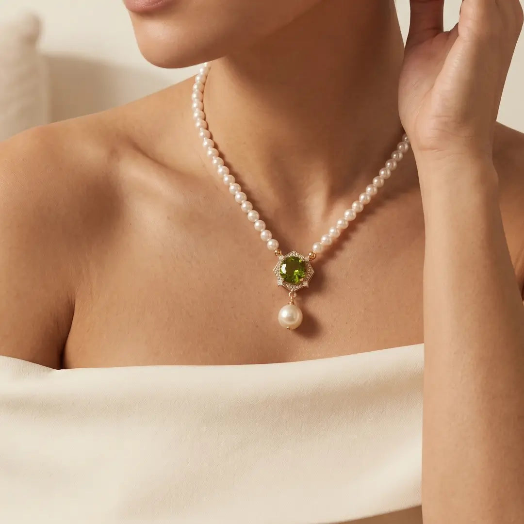Aiko Tanaka Hasuike necklace, a pearl strand with a gold-set green stone and pearl, worn by a model in cream