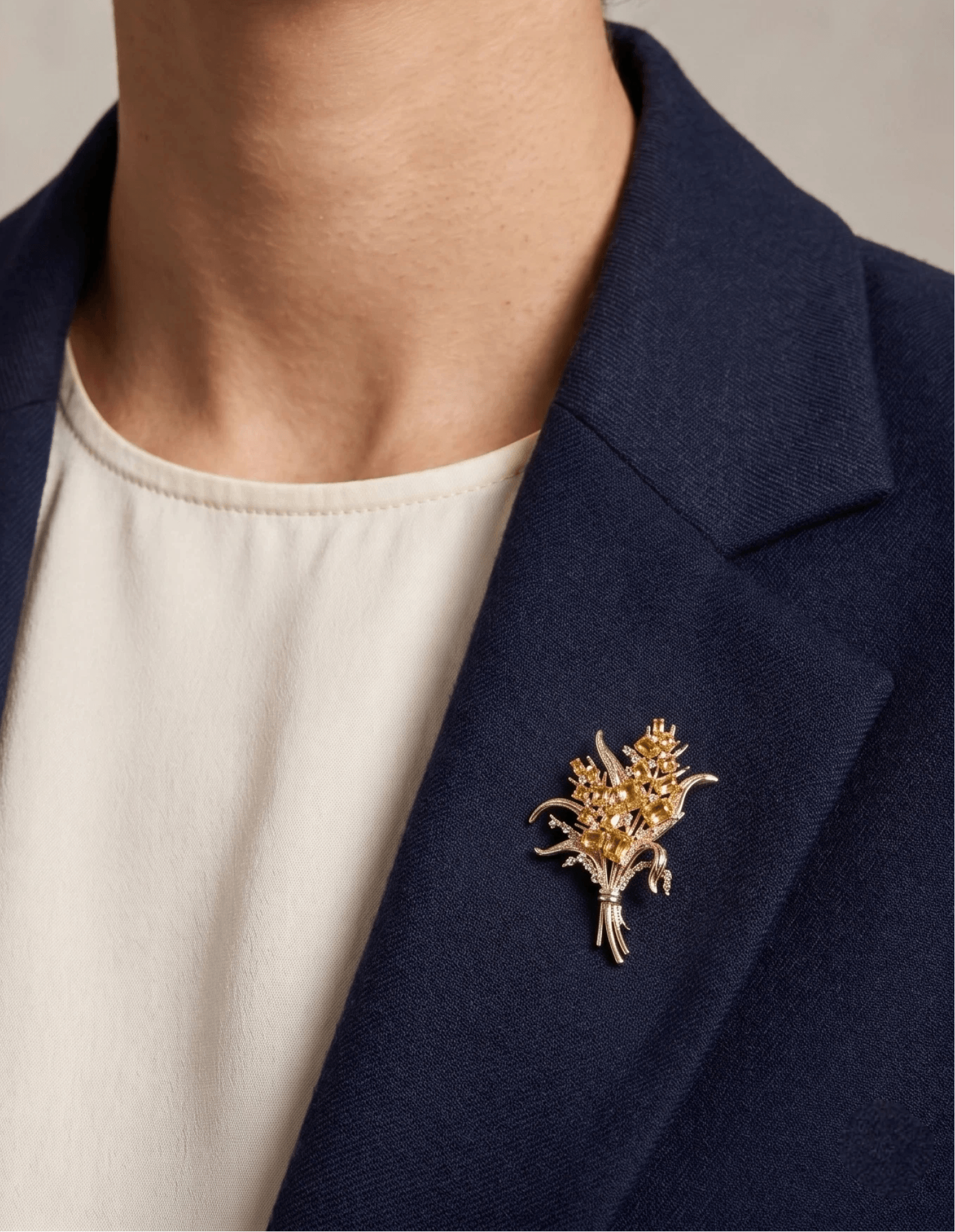 Woman in a navy blazer over a cream top wearing the Aiko Tanaka Kogane no Minori gold crystal spray brooch