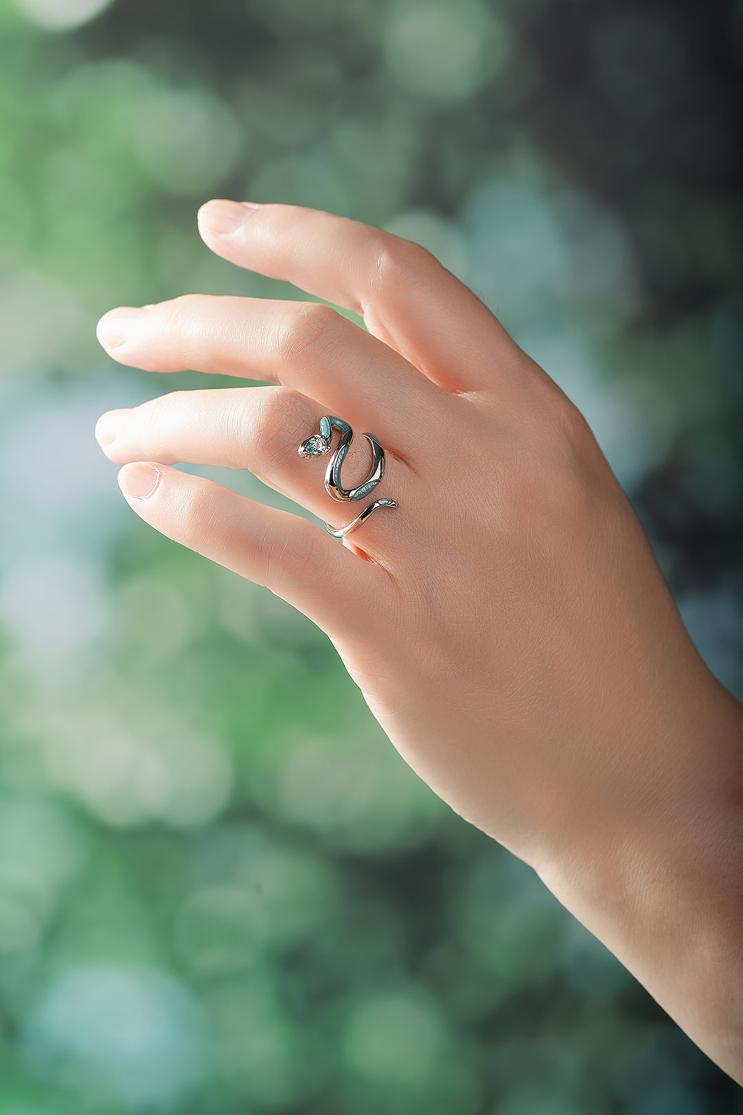 Hand against soft green foliage wearing the Aiko Tanaka Hebi no Nami silver and enamel coiled snake ring