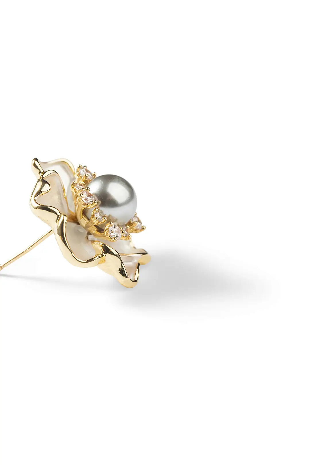 Side view of an Aiko Tanaka Koharu earring, a mother-of-pearl flower with a grey pearl center, on white