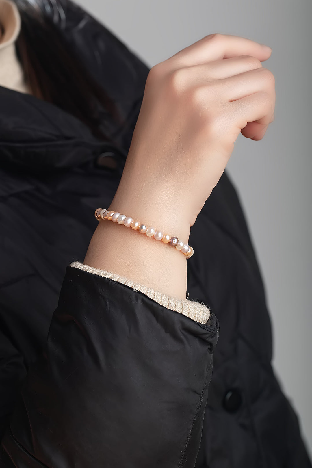 Wrist in a black puffer jacket wearing the Aiko Tanaka Nagomi multicolor freshwater pearl stretch bracelet