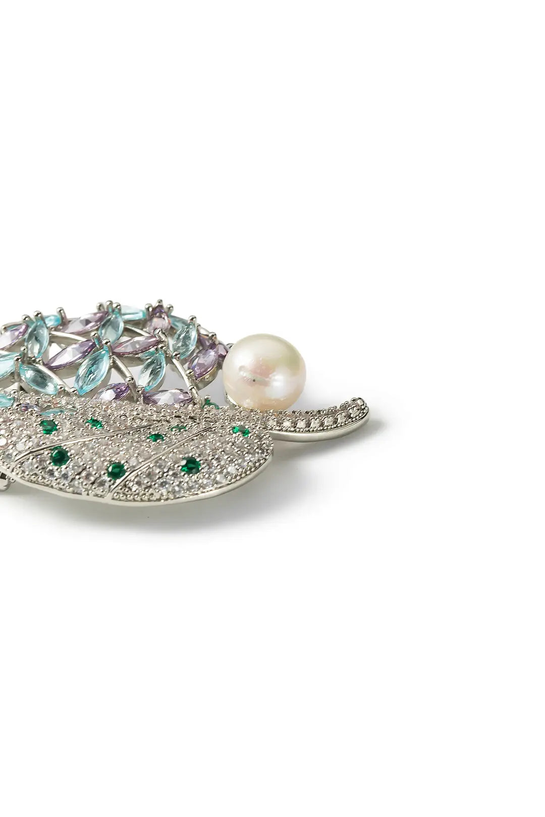 Aiko Tanaka Shion brooch side view, a crystal leaf with green stones and a white pearl, on a white background