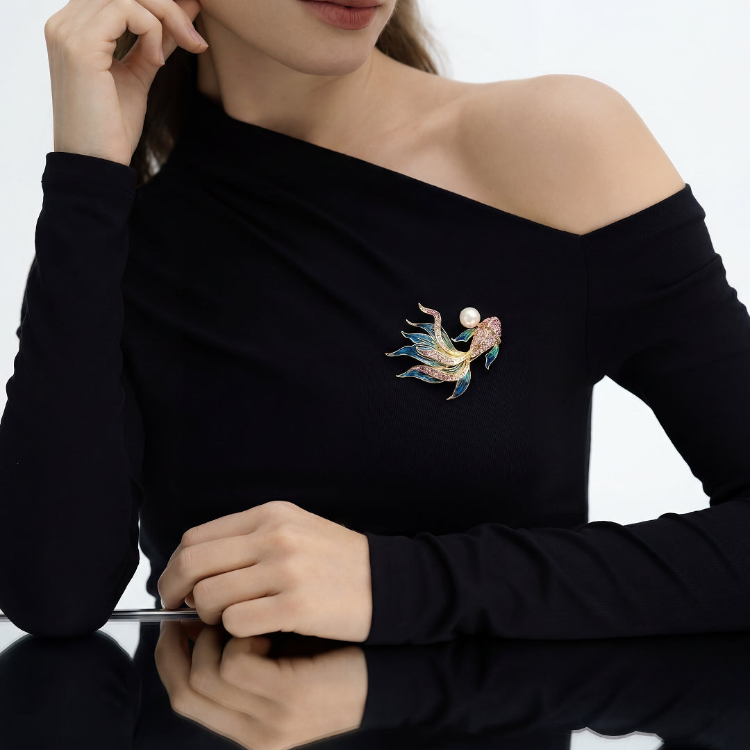 Woman in a black off-shoulder top wearing the Aiko Tanaka Nishiki no Yume koi brooch with a pearl, seated at a table