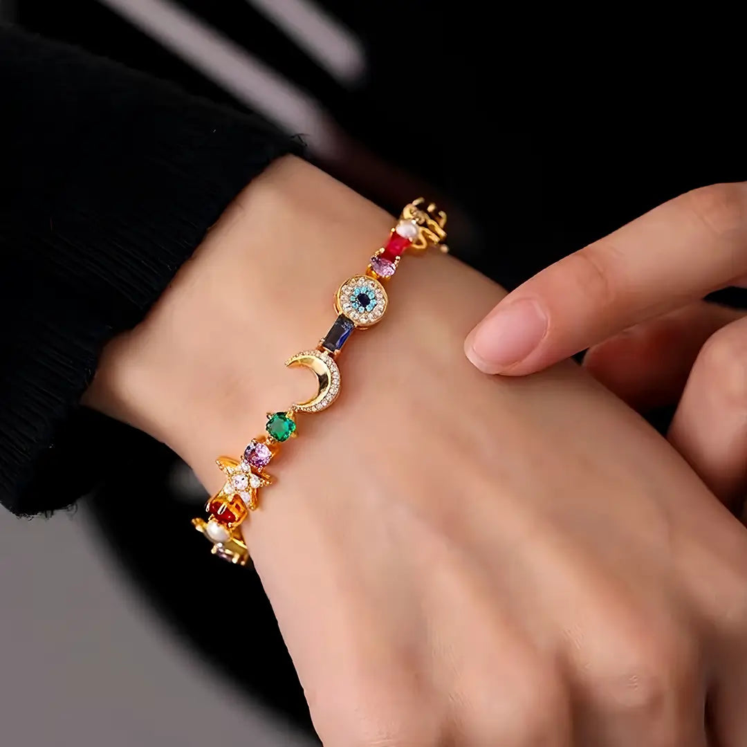Close-up of a wrist wearing the Aiko Tanaka Omamori gold charm bracelet with moon, heart and gem charms