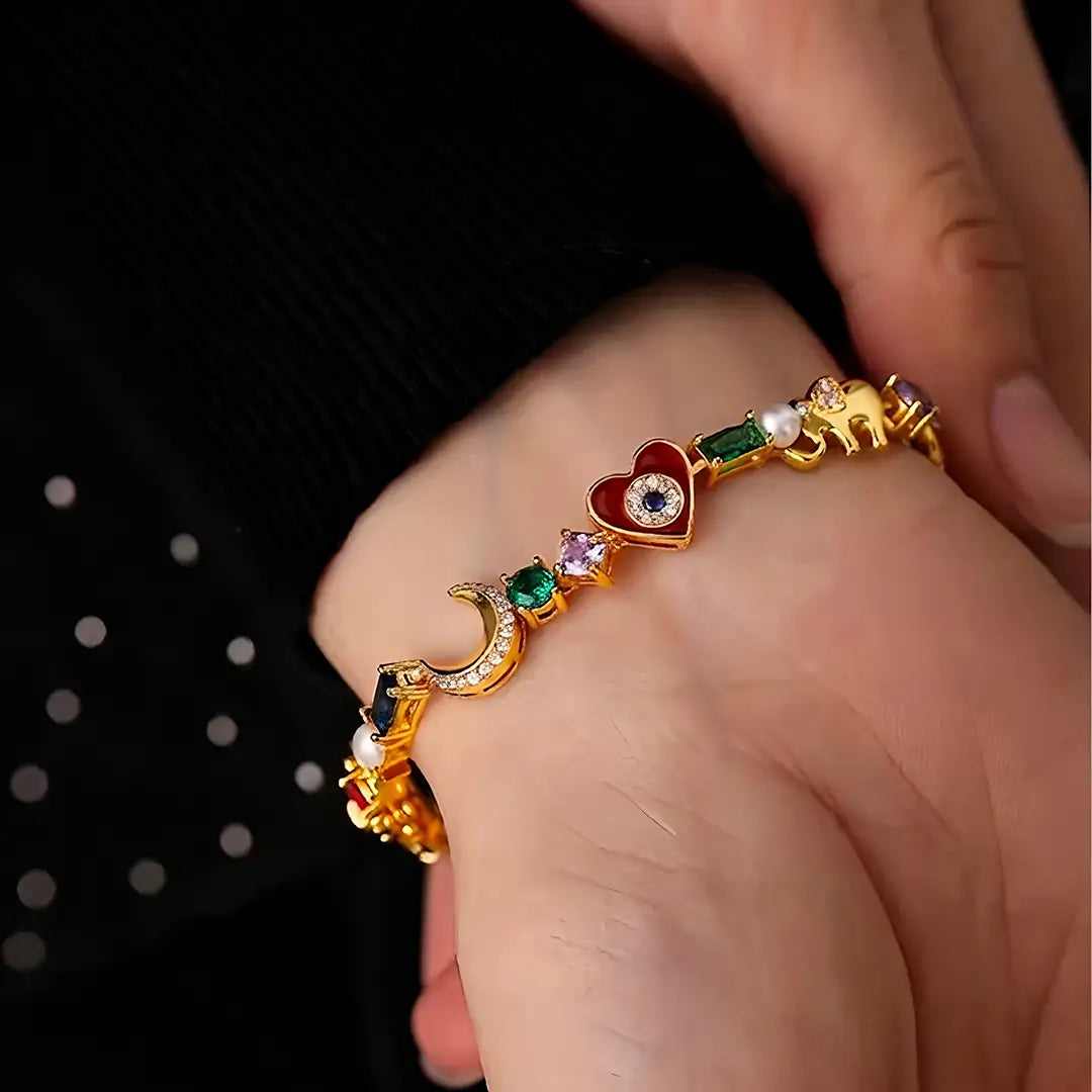 Wrist in a black sleeve wearing the Aiko Tanaka Omamori gold charm bracelet with a red heart and colored stones