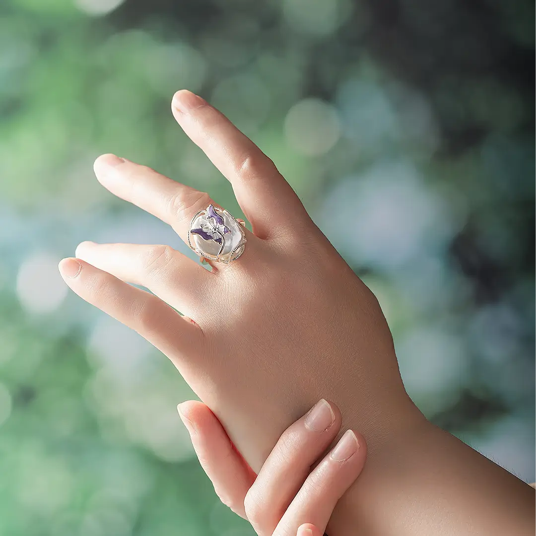 Hand against green foliage wearing the Aiko Tanaka Casane silver ring with a sculpted mother-of-pearl face