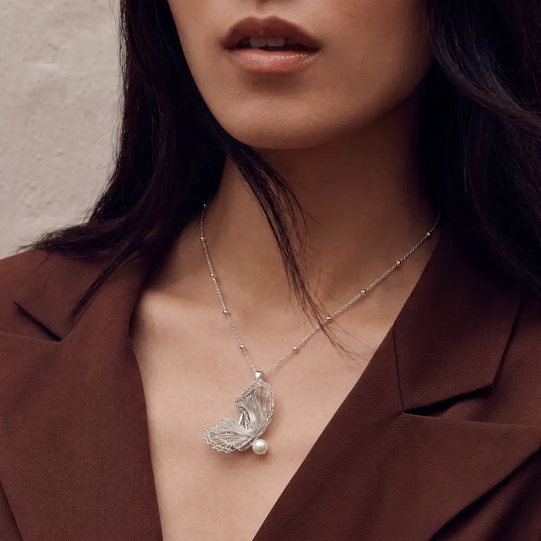 Aiko Tanaka Hakucho necklace, a silver wing and pearl pendant, worn by a model in a brown V-neck top