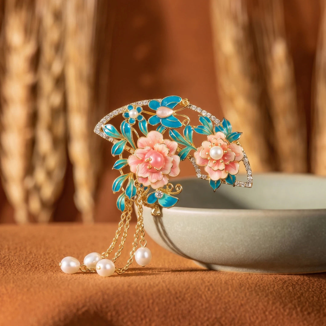 Aiko Tanaka Hanagasumi fan brooch with pink blossoms and pearl tassels beside a ceramic bowl and dried wheat
