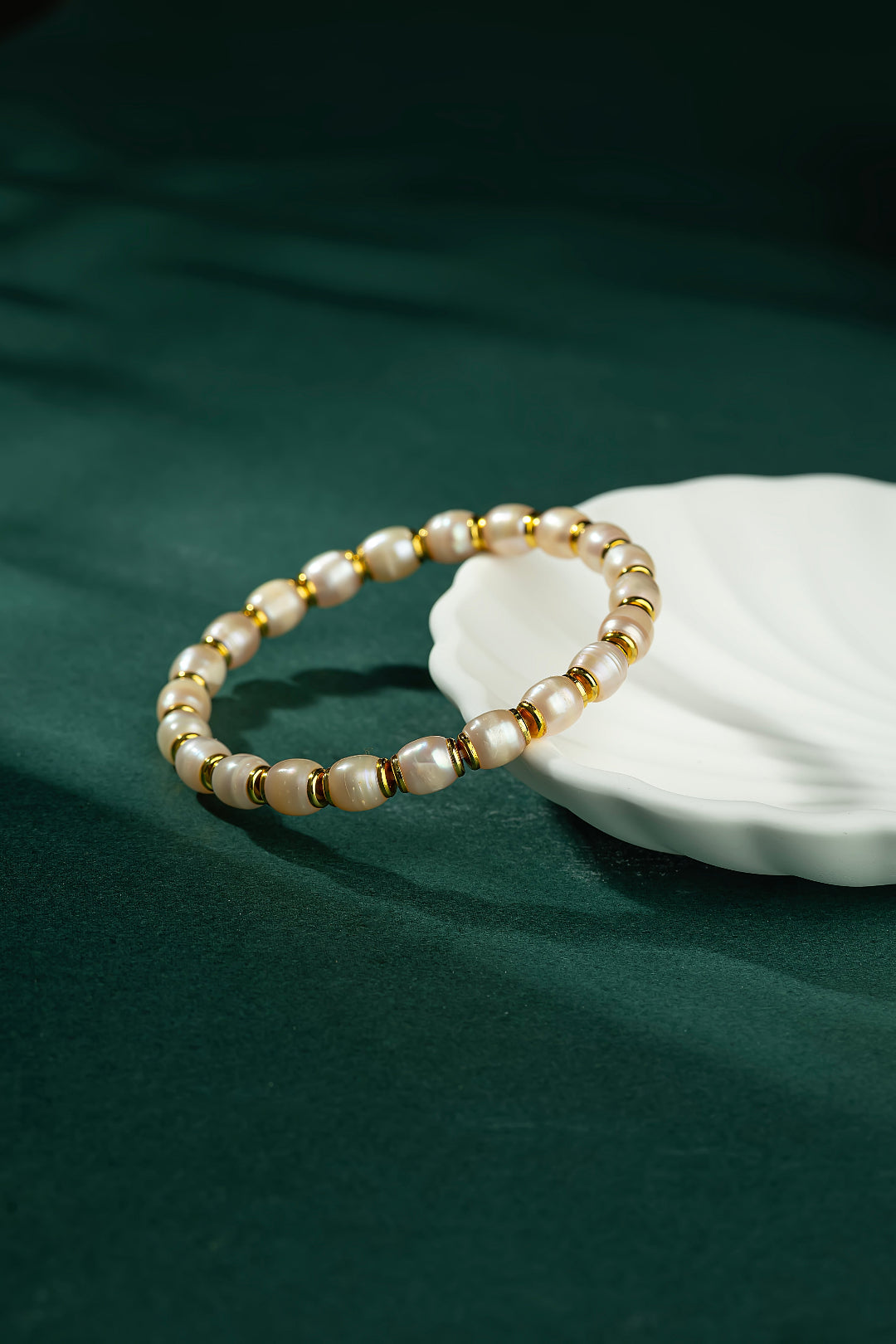 Aiko Tanaka Hinata pearl and gold bead bracelet resting on deep green velvet beside a white ceramic shell dish