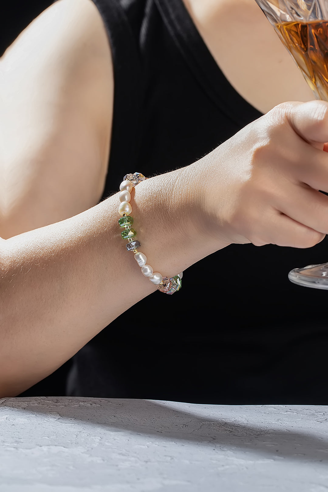 Woman in a black tank top holding a glass, wearing the Aiko Tanaka Hoshi no Kakera pearl and crystal bracelet