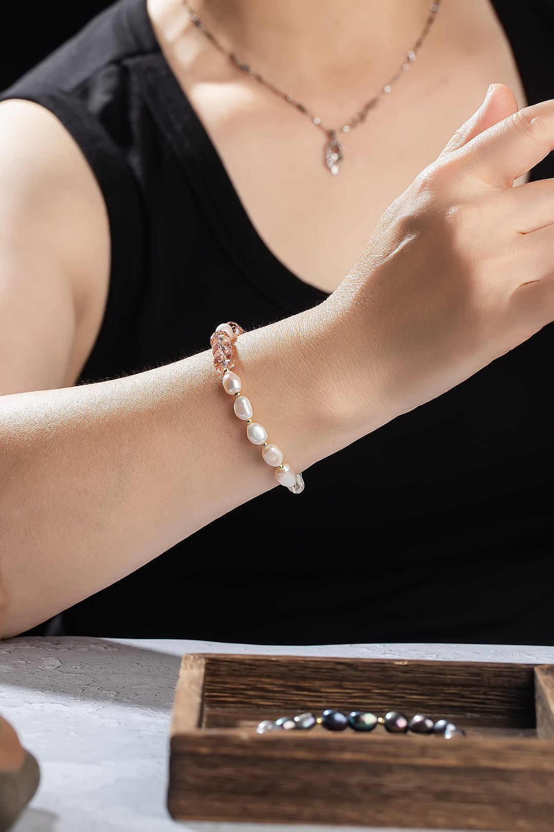 Woman in a black tank top wearing the pink Aiko Tanaka Hoshi no Kakera pearl bracelet with a pendant necklace