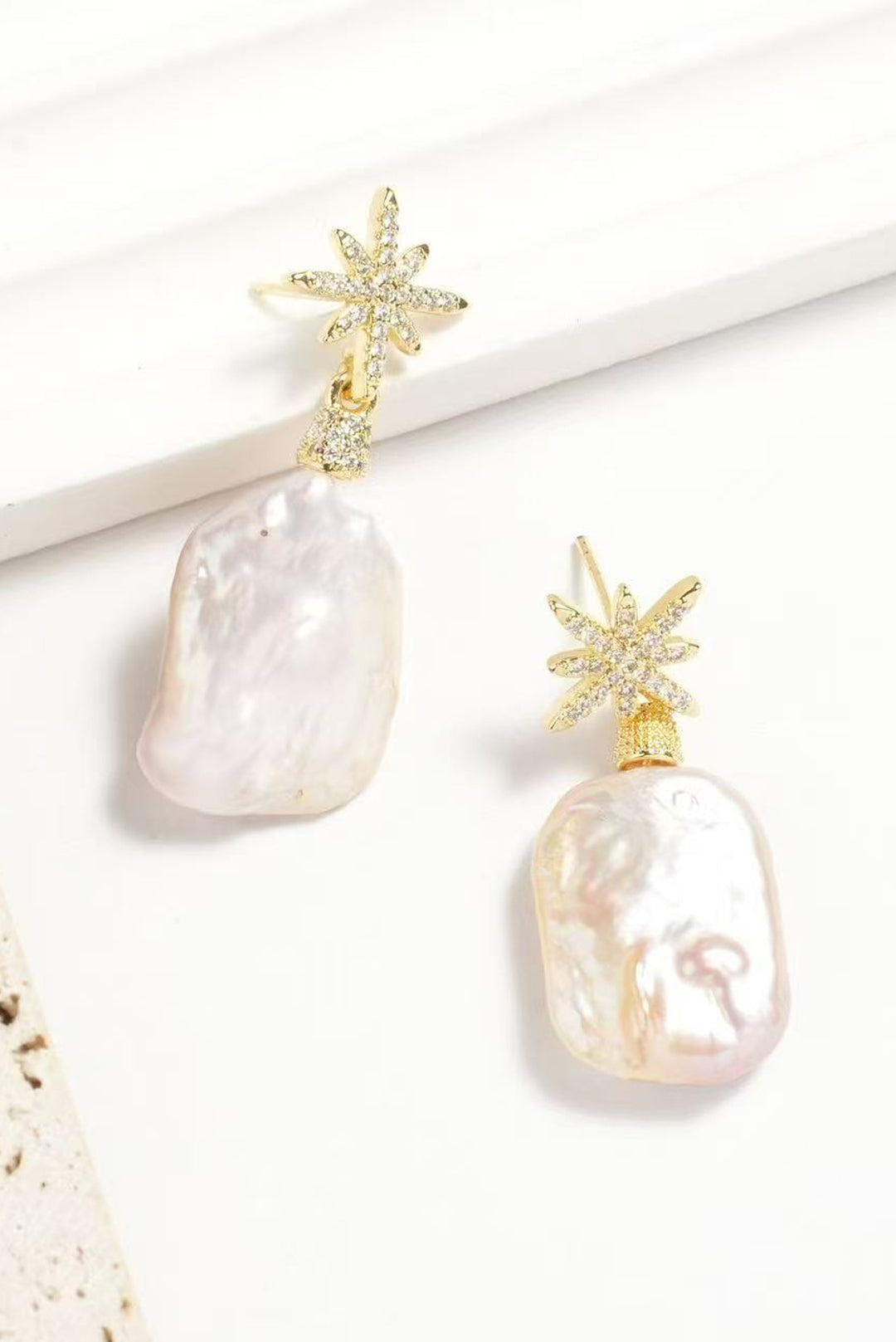 Aiko Tanaka Hoshi no Kakera baroque pearl drop earrings with gold crystal star tops, displayed on a white stand