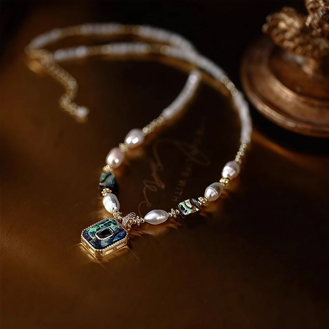 Aiko Tanaka Kai no Hoseki pearl and abalone necklace laid on a warm brown surface beside a vintage gold ornament