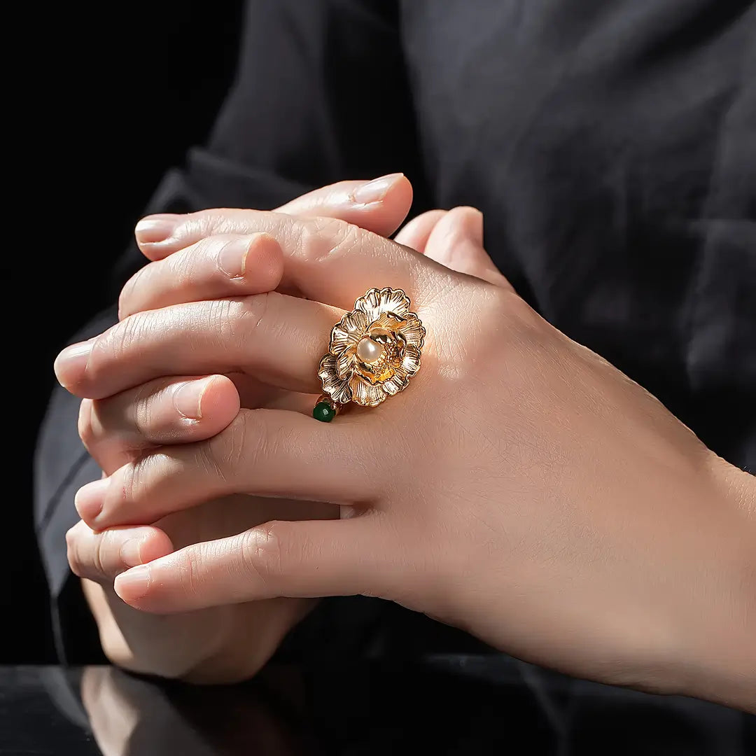 Aiko Tanaka Kinsenka ring worn on a finger, a gold sculpted flower ring with a pearl, hands clasped together