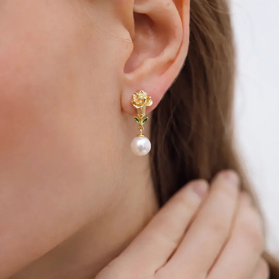 Aiko Tanaka Kinuoto earrings worn on the ear, a gold flower stud with a white pearl drop, hand at the jaw