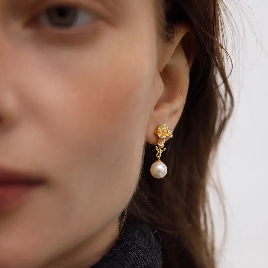 Aiko Tanaka Kinuoto earrings, a gold flower stud with a white pearl drop, worn by a model with brown hair