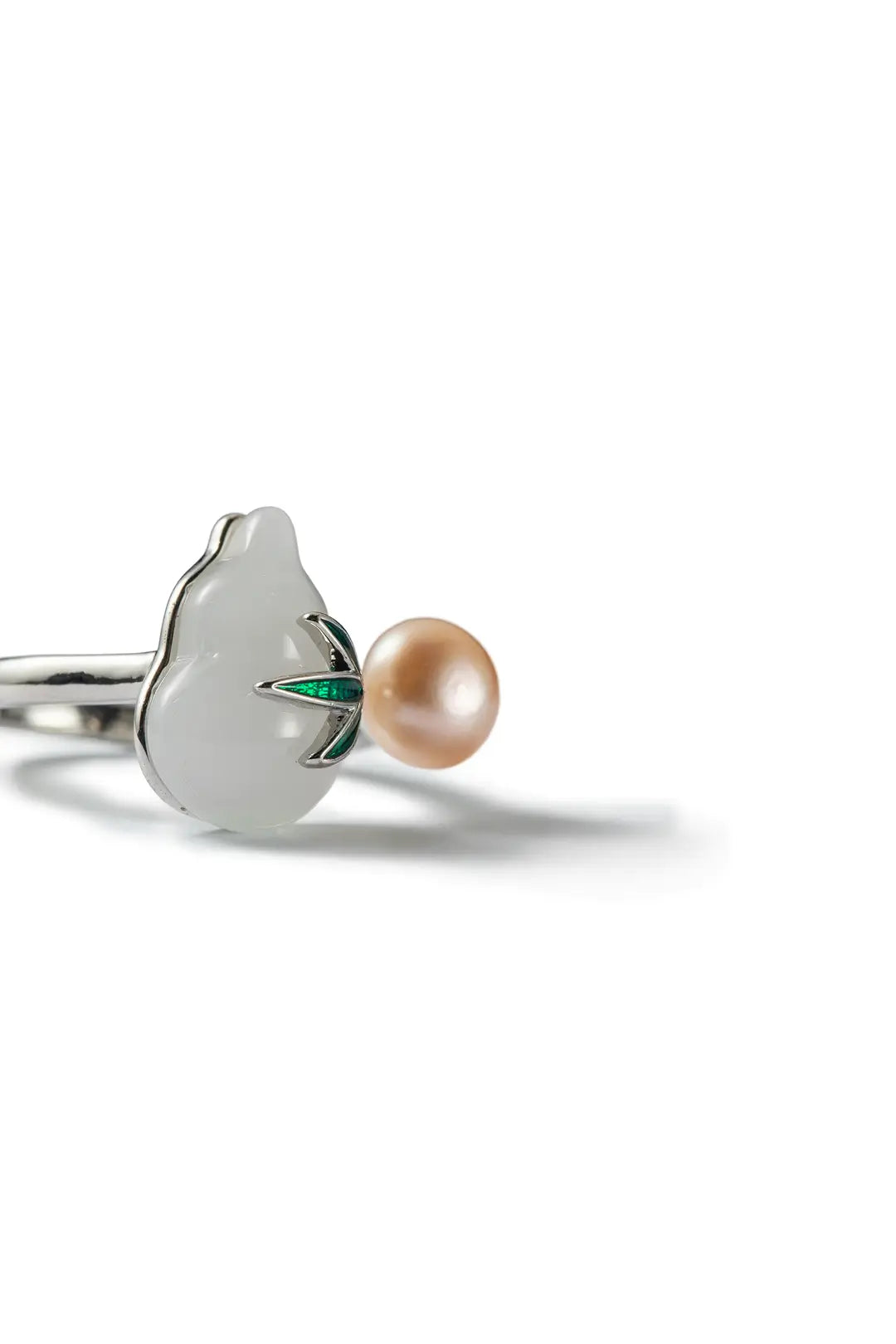 Aiko Tanaka Kissho ring close-up, a white enamel gourd with green leaf beside a peach pearl, on a white background