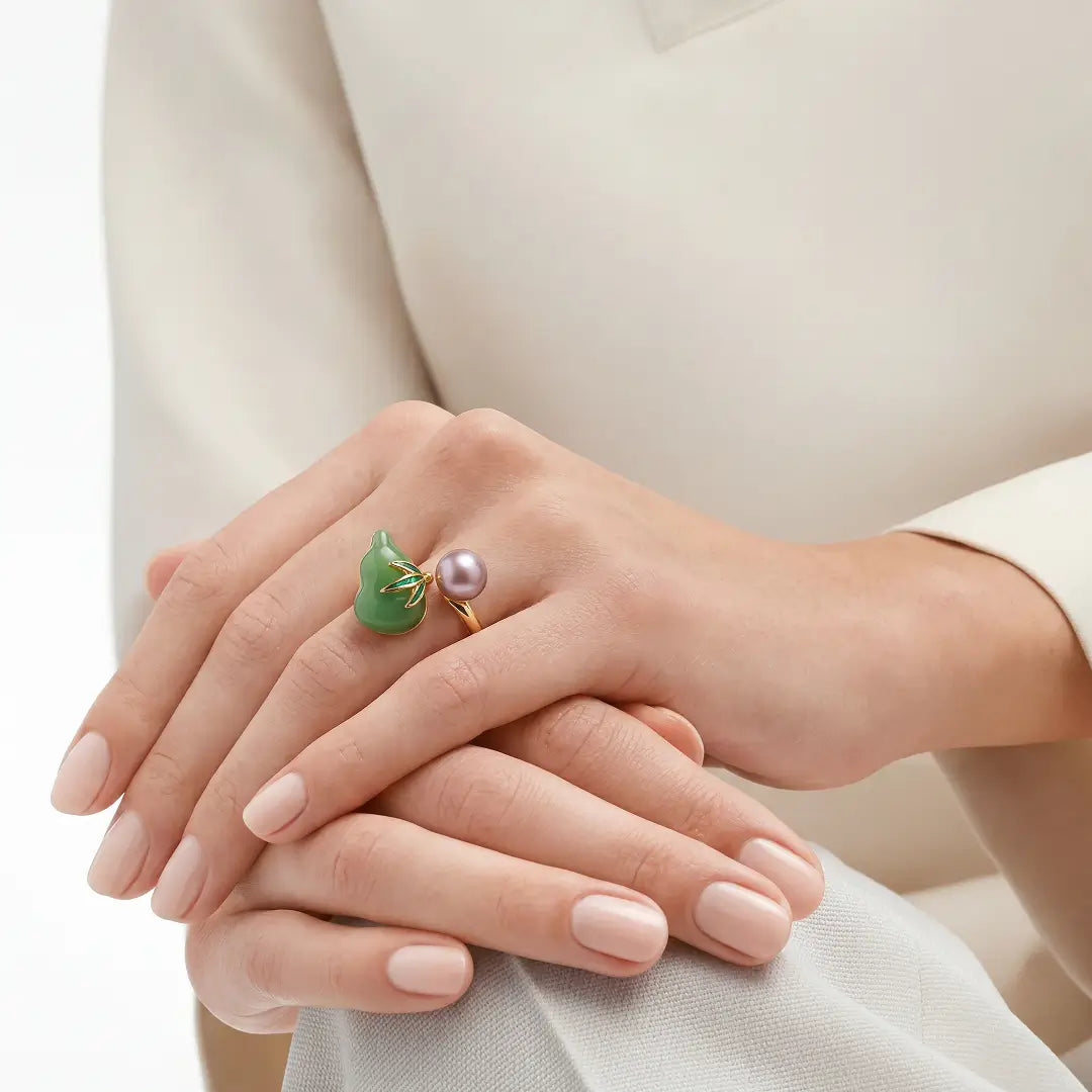 Hands resting on a cream sleeve wearing the Aiko Tanaka Kissho jade gourd and pink pearl ring
