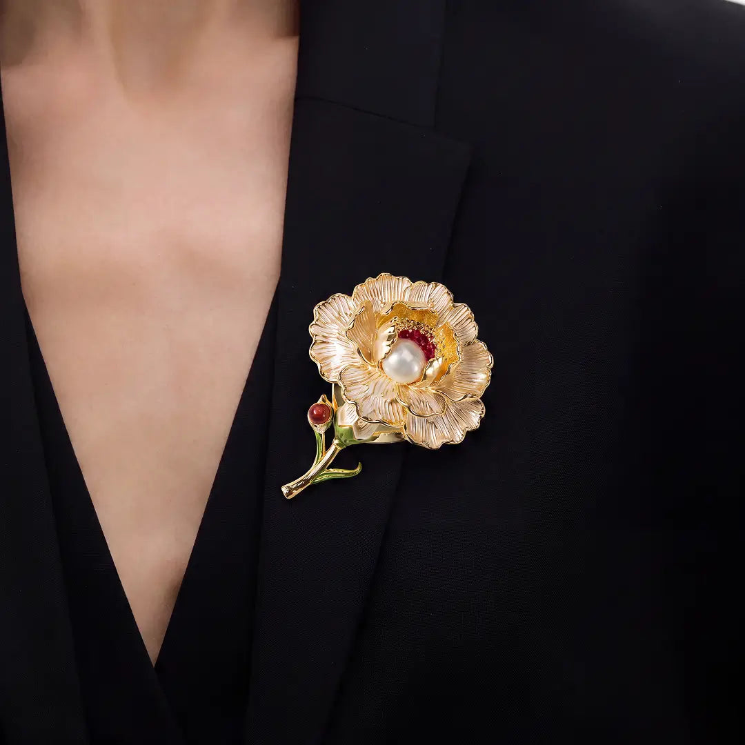 Aiko Tanaka Kohaku no Niwa brooch, a gold flower with a pearl and red stone center, worn on a black V-neck top