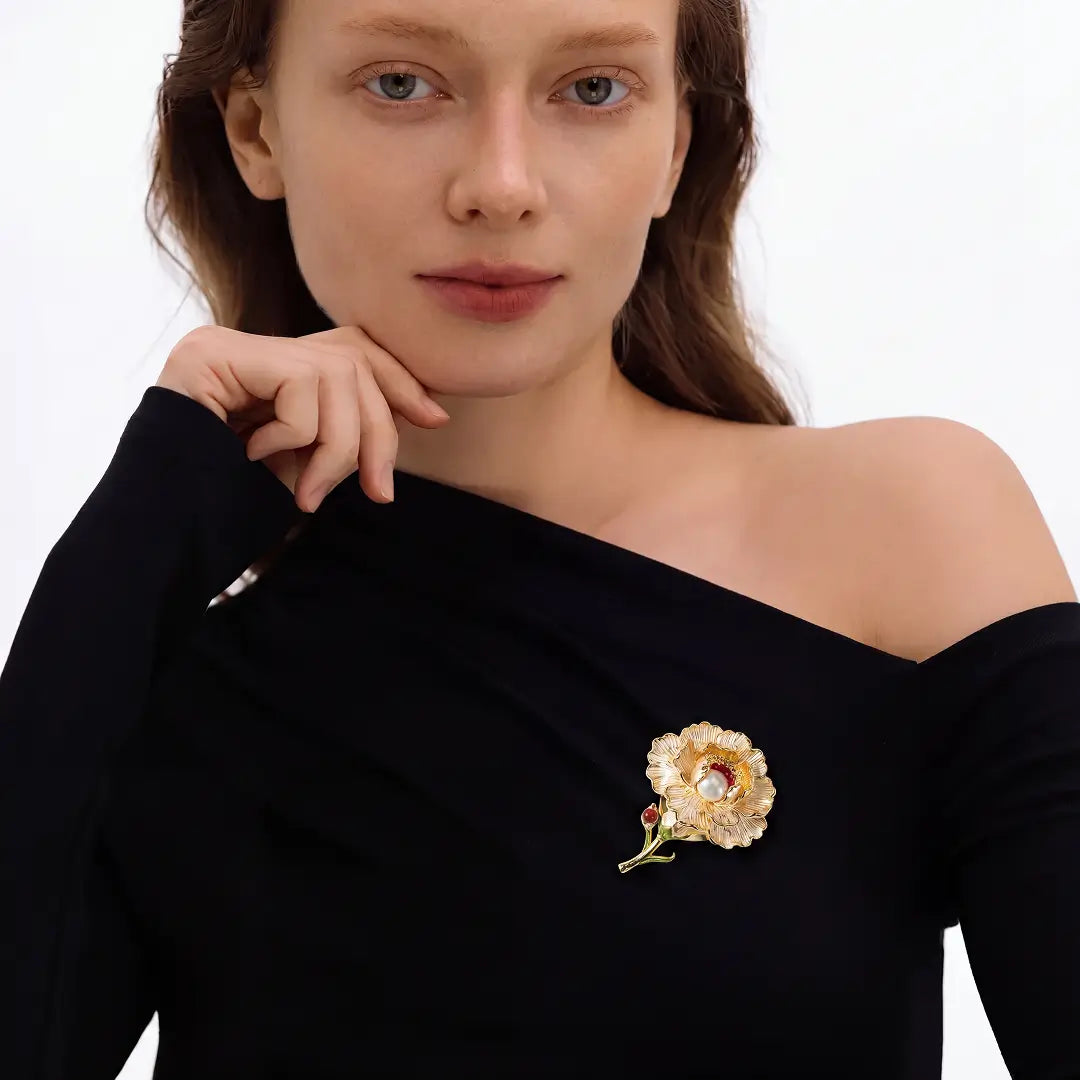 Aiko Tanaka Kohaku no Niwa brooch, a gold flower brooch, pinned to a black off-shoulder top worn by a model