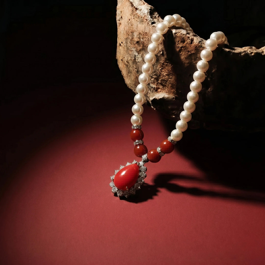 Aiko Tanaka Kokei pearl necklace with a red teardrop pendant draped over driftwood on a dark red background