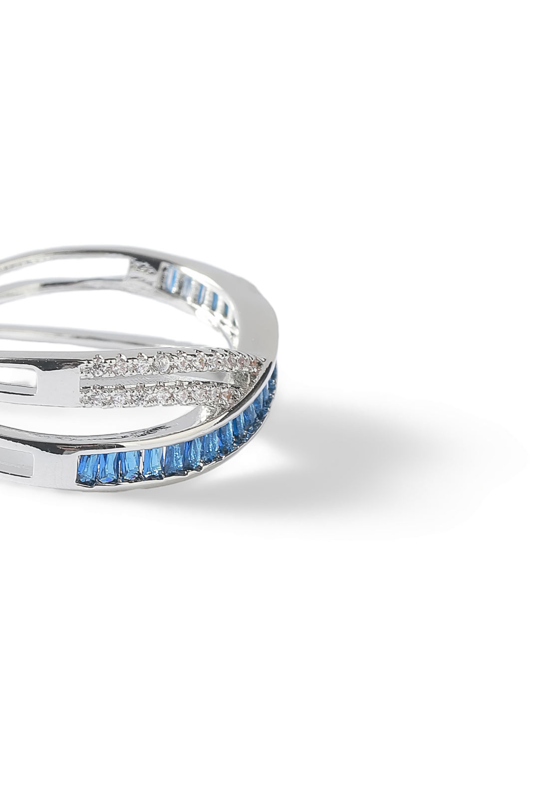 Aiko Tanaka Kosa ring, a silver crossover band of pave crystals and blue stones, side view on a white background