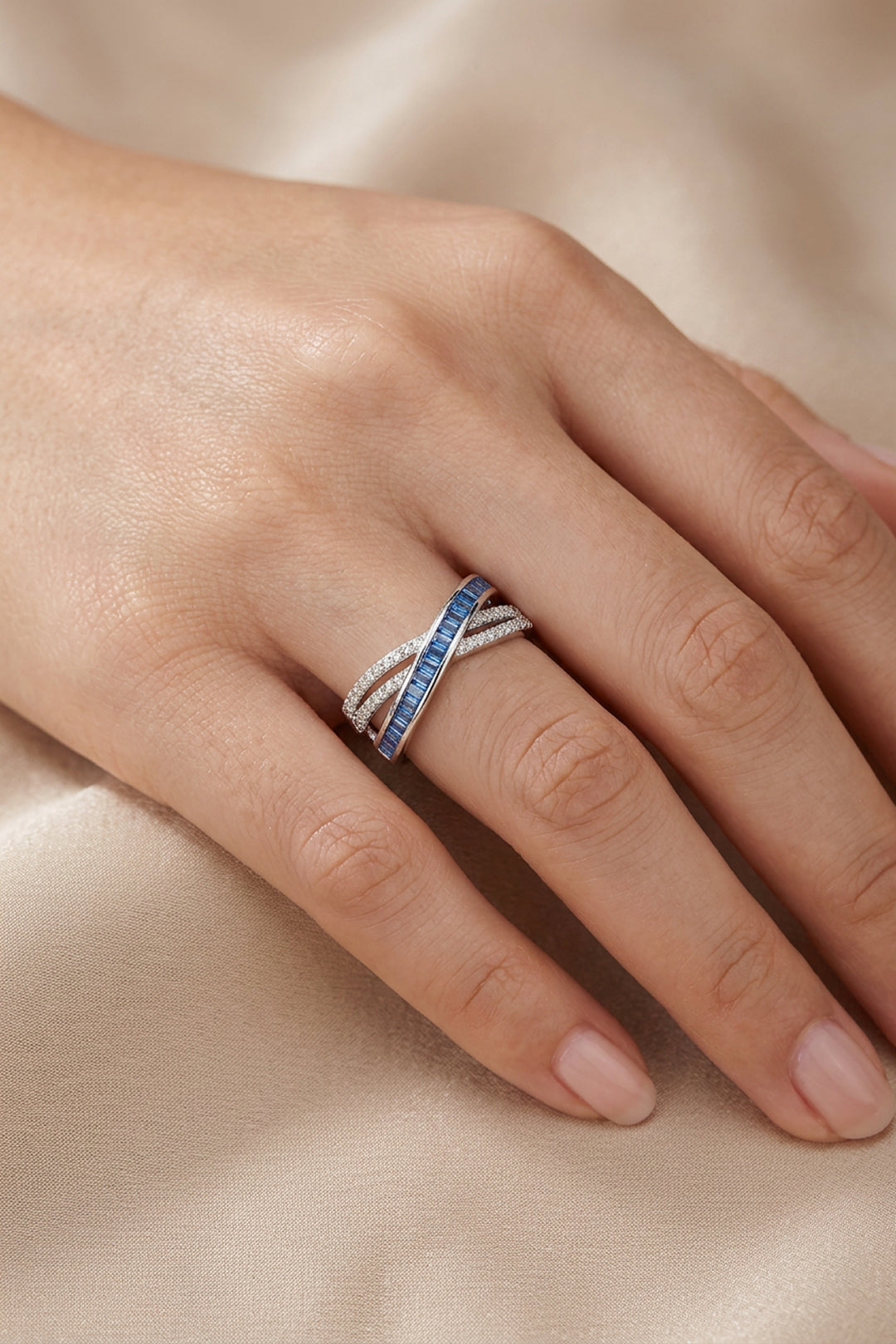 Hand on a beige surface wearing the Aiko Tanaka Kosa crossover ring with blue stones and pave crystals