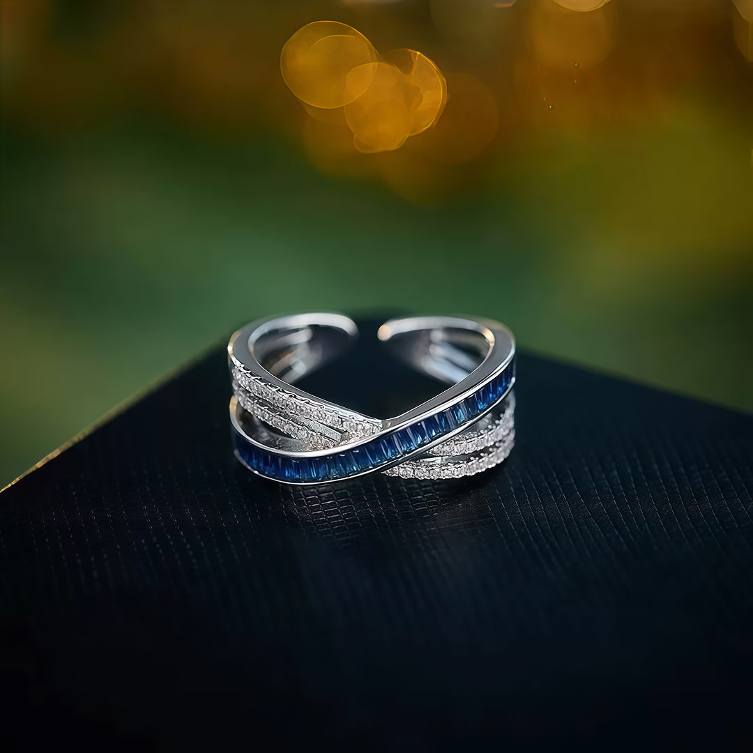 Aiko Tanaka Kosa silver crossover ring with rows of blue stones displayed on a dark ledge with golden bokeh