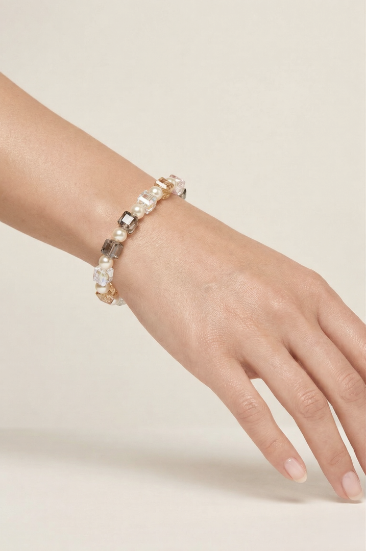 Wrist wearing the Aiko Tanaka Kosai no Wa bracelet of white pearls and pastel crystal cubes against a cream backdrop