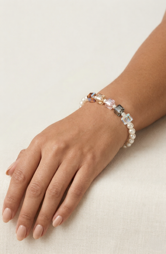 Hand resting on a table wearing the Aiko Tanaka Kosai no Wa pearl and crystal cube bracelet against a neutral backdrop