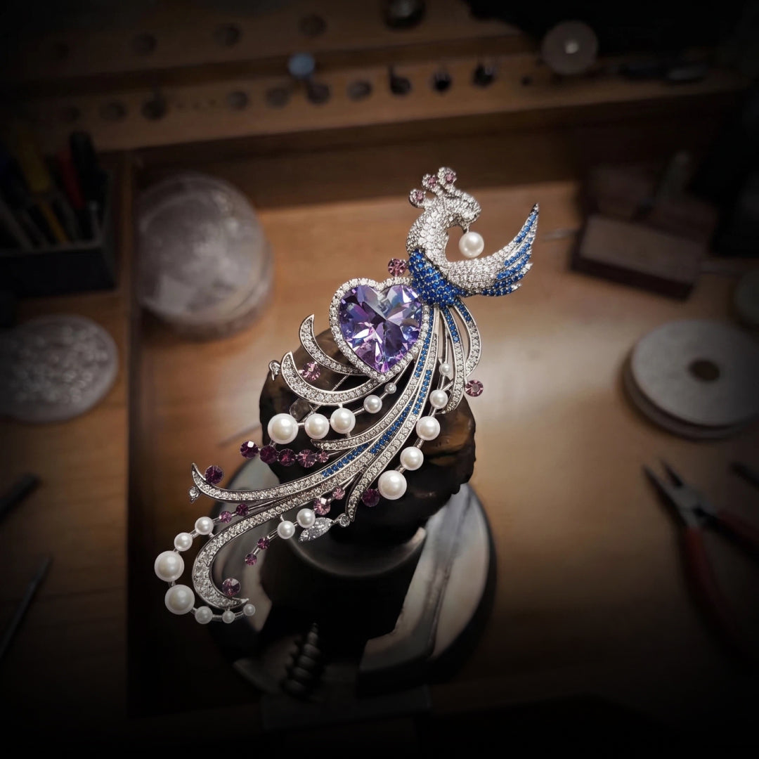 Aiko Tanaka Kujaku no Shingetsu peacock brooch with pearls and a lilac heart stone displayed on a jeweler's workbench