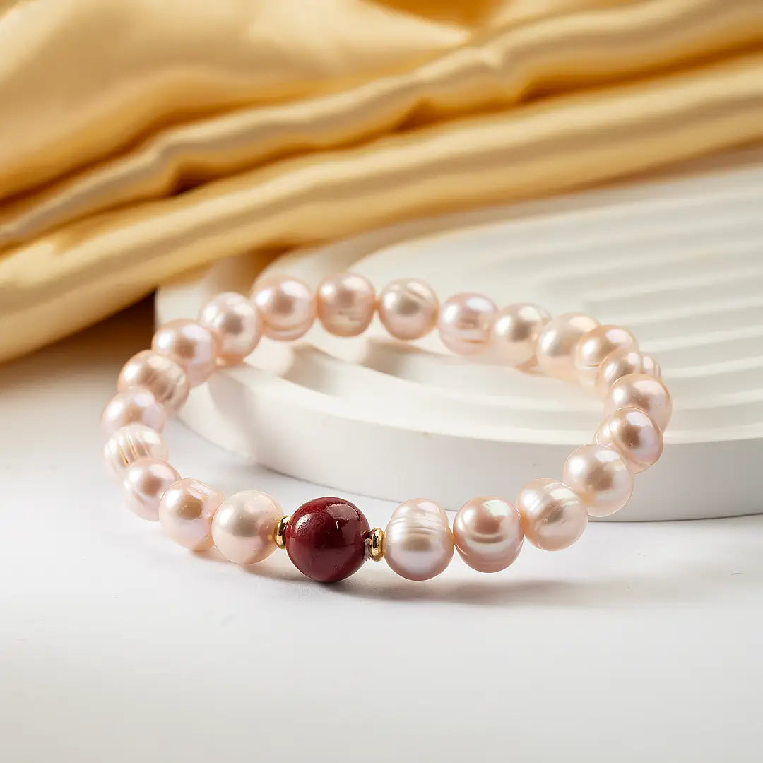 Aiko Tanaka Kurenai bracelet, a pink freshwater pearl stretch bracelet with a red bead, resting on gold silk