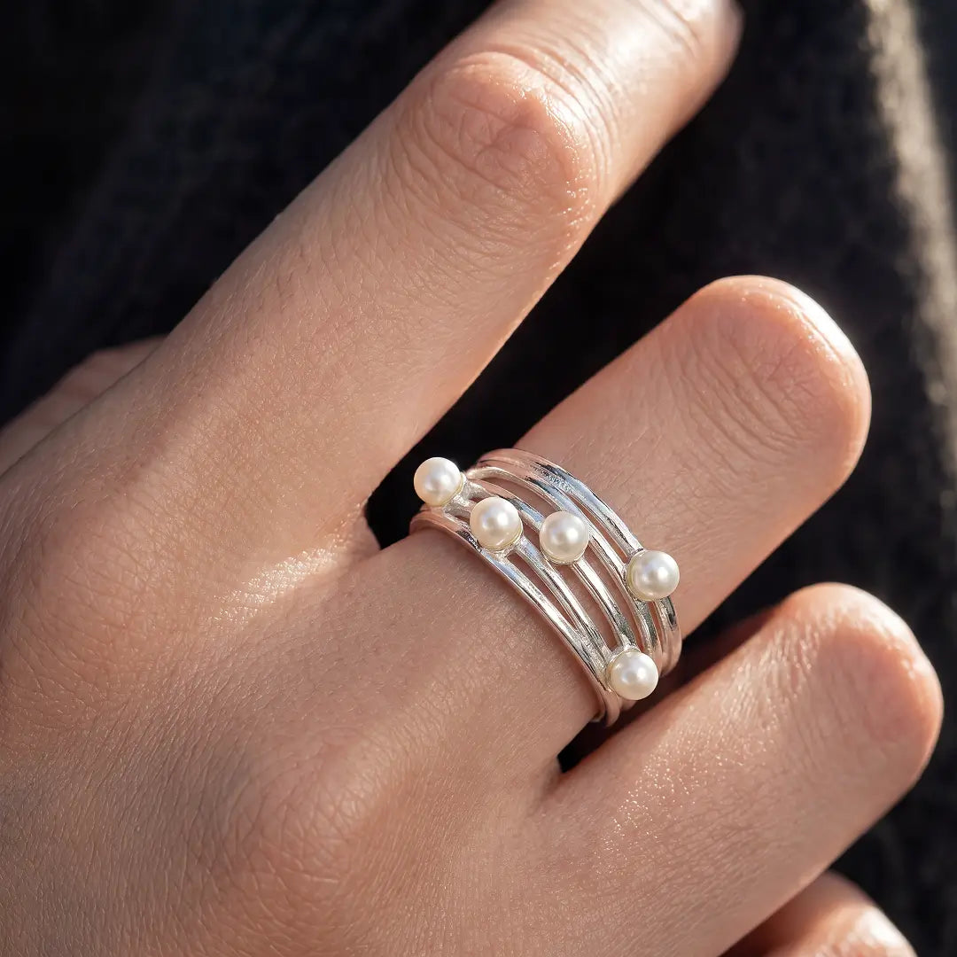Aiko Tanaka Meguri ring, a silver woven band ring with small pearls, worn on the hand against a dark sweater