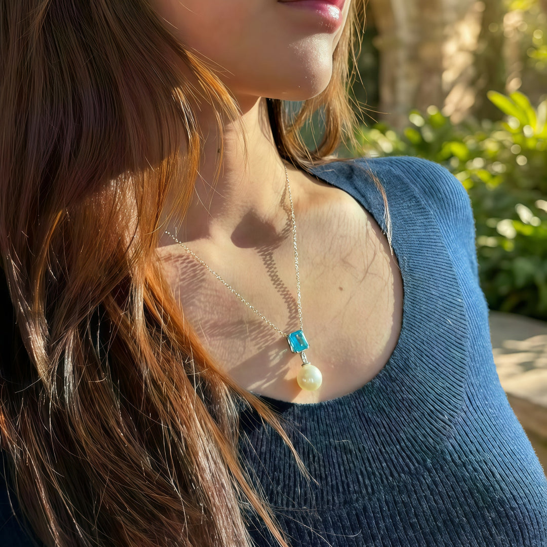 Close-up of the Aiko Tanaka Mizu Fracture necklace, a white pearl drop below an aqua blue stone, worn over a knit top