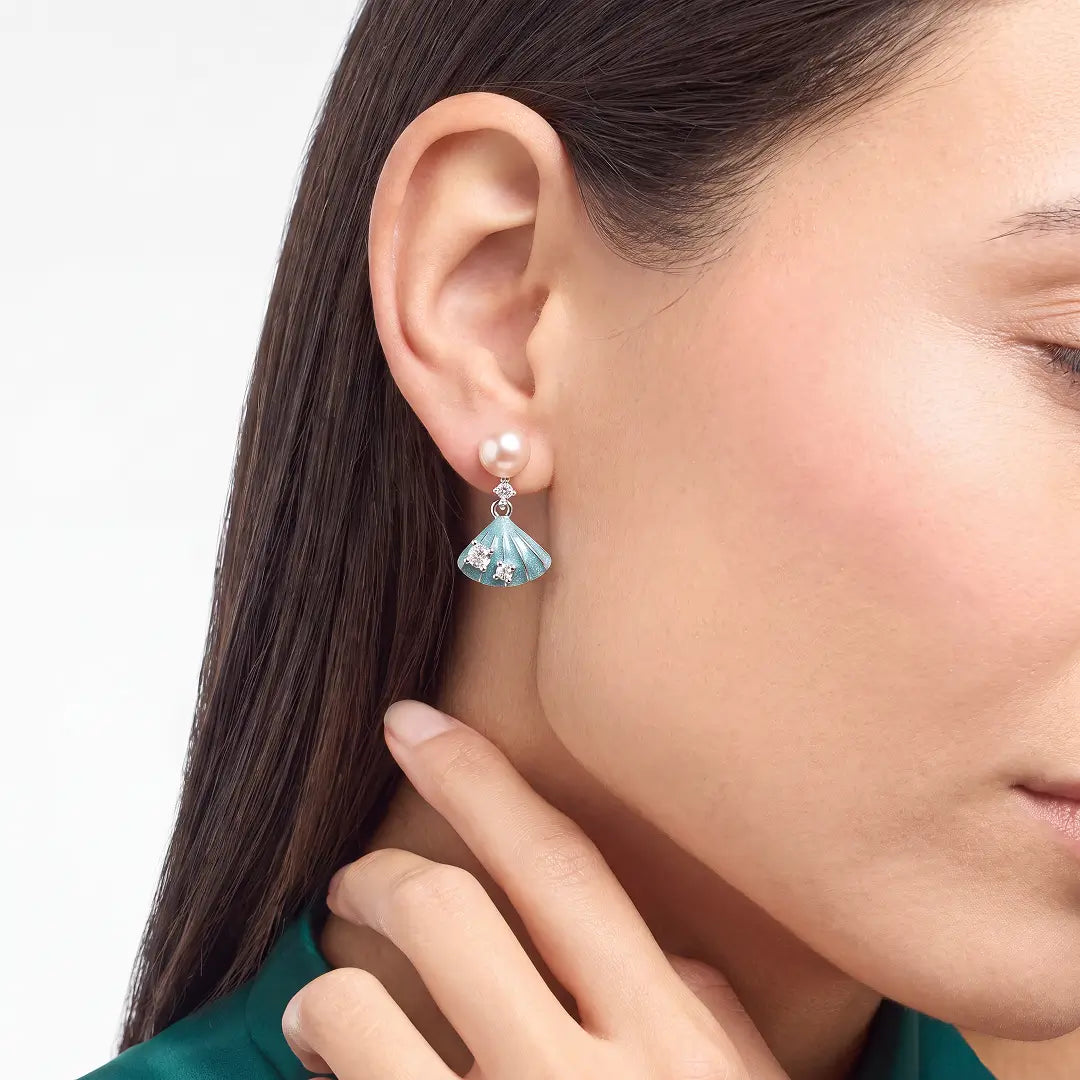 Aiko Tanaka Nagisa earrings worn on the ear, a peach pearl stud with a blue enamel shell drop, hand at the neck