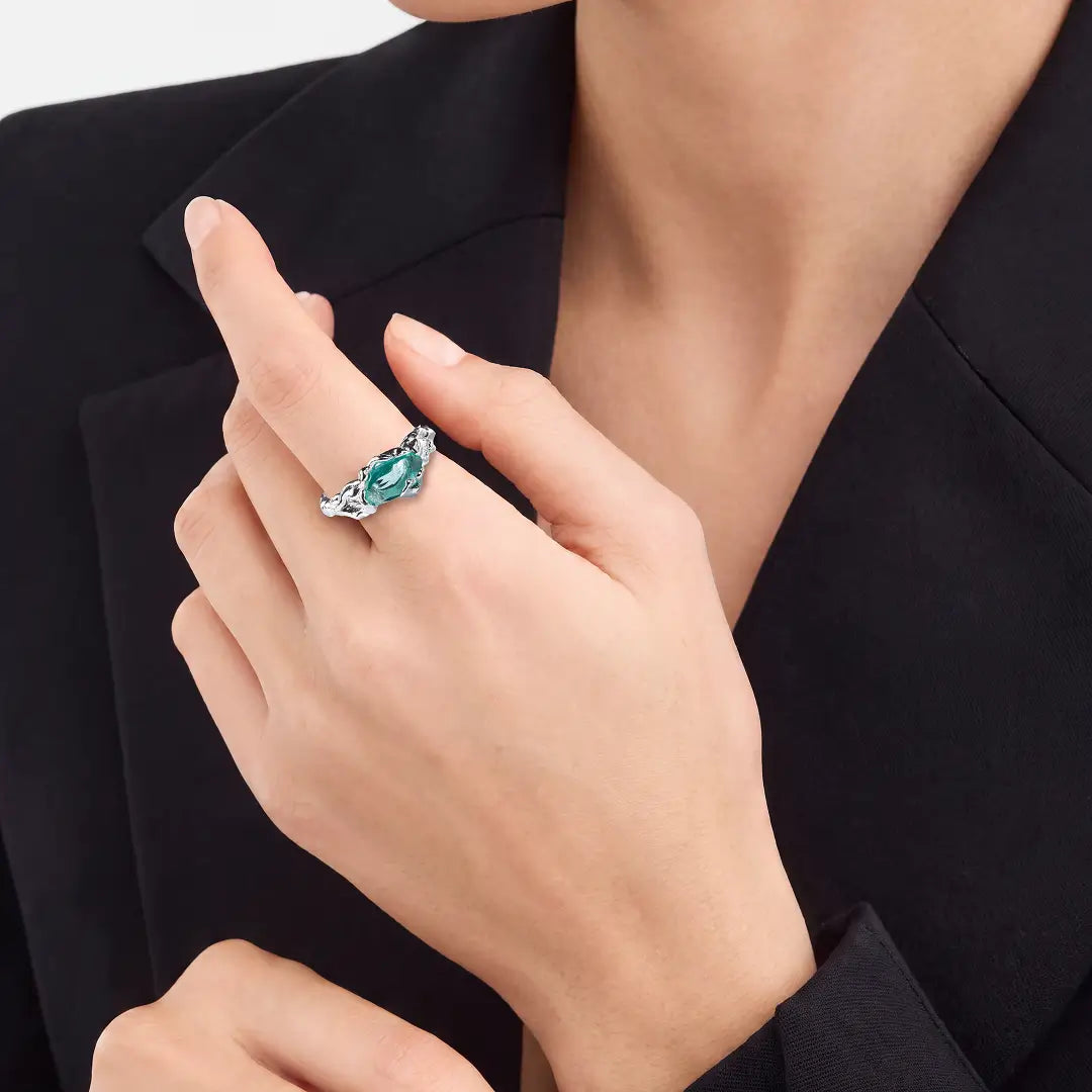 Aiko Tanaka Nami no Suisei ring, a silver wave ring with a teal stone, worn on the hand against a black blazer