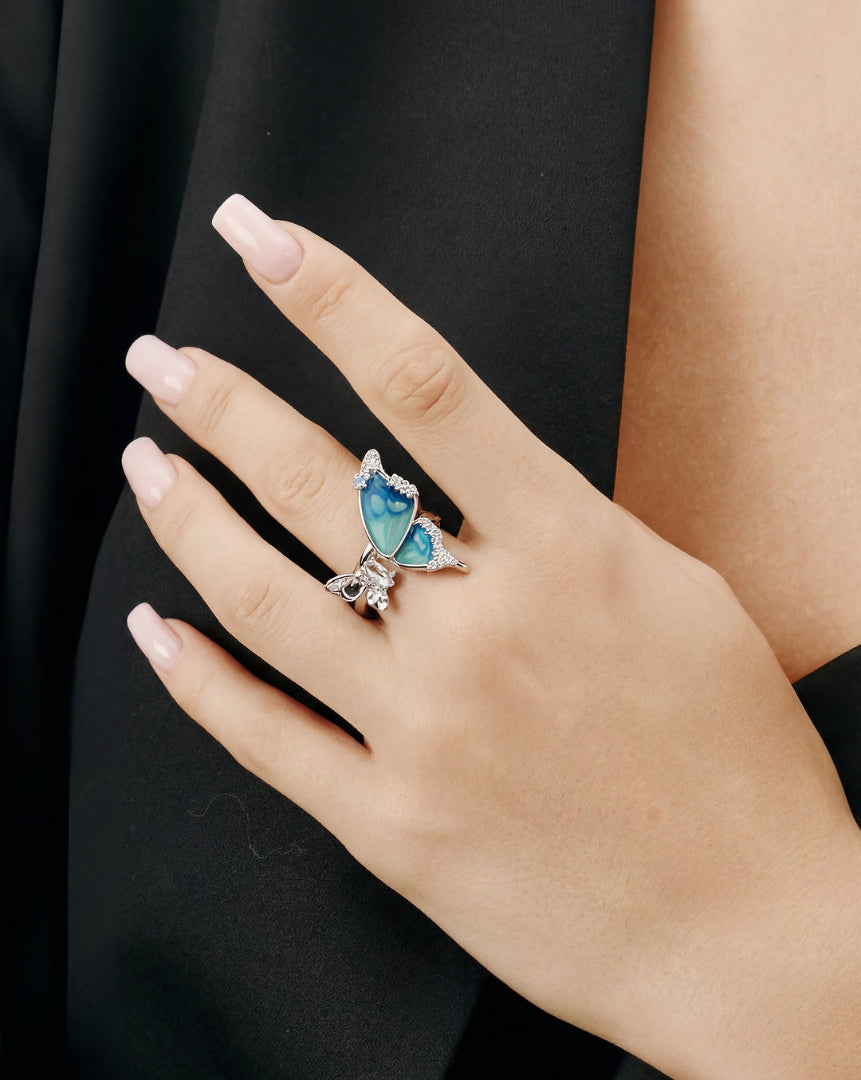 Hand resting on a black sleeve wearing the Aiko Tanaka Ran no Cho silver ring with a blue enamel butterfly