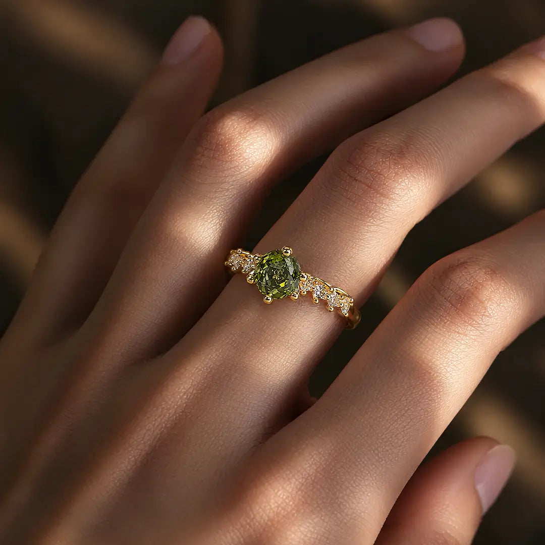 Aiko Tanaka Rensei ring, a gold band set with a green stone and small crystals, worn on a hand in warm light