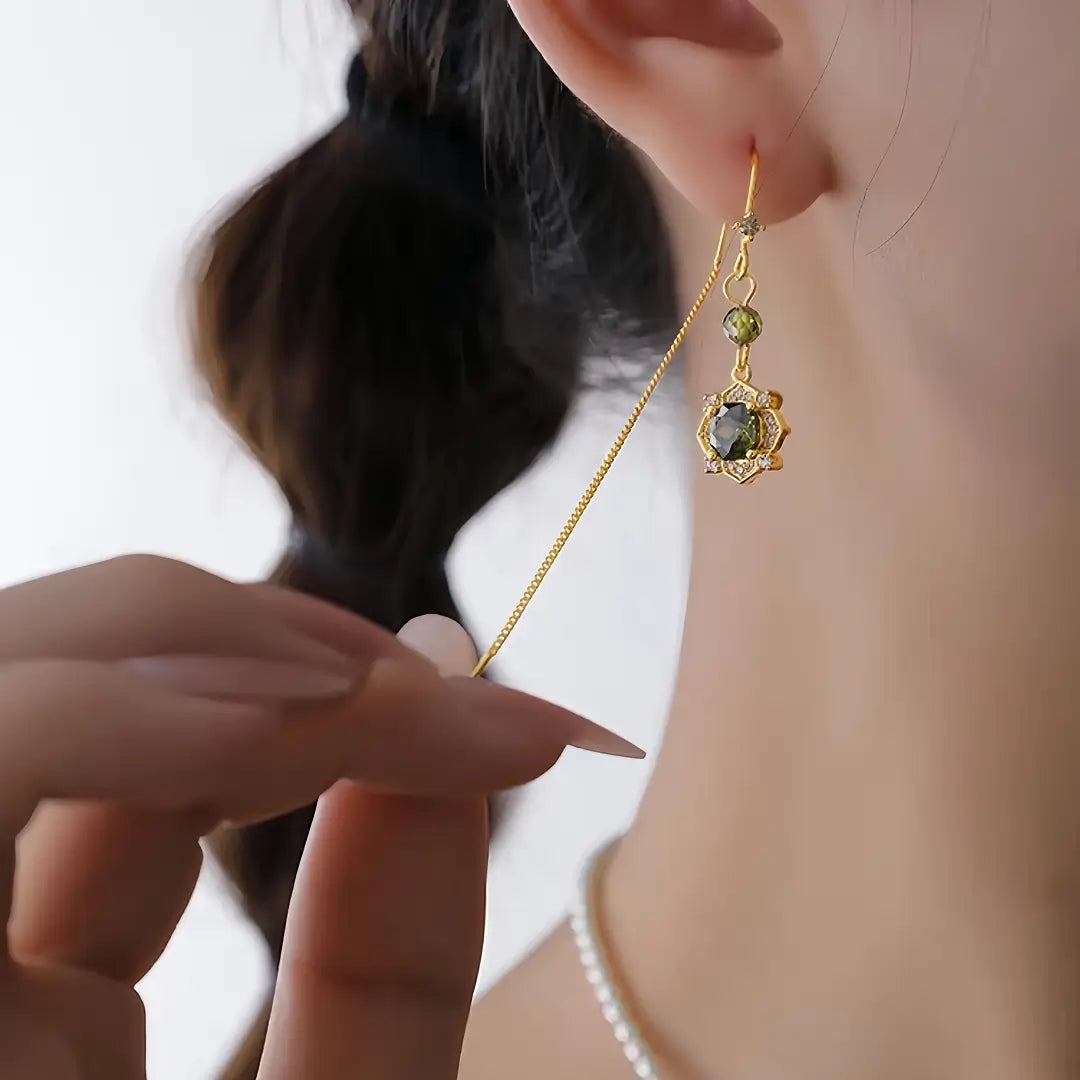 Aiko Tanaka Rensui earrings, a gold threader with green stones, being adjusted at the ear by a model's hand