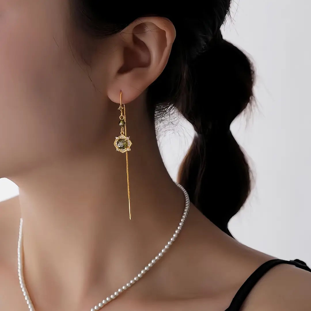Aiko Tanaka Rensui earrings, a long gold threader with a green stone flower, worn by a model with braided hair