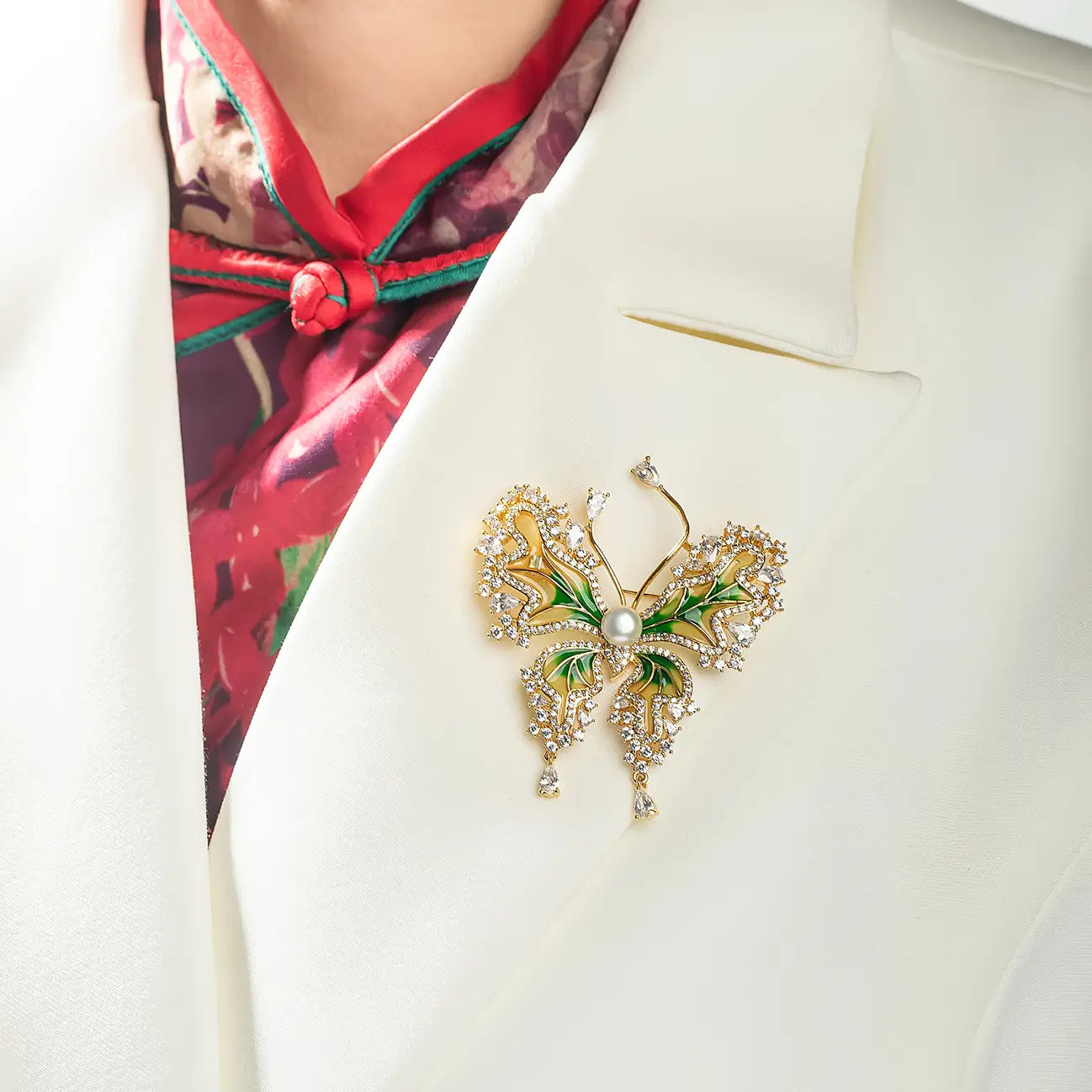 Woman in a white blazer over a red top wearing the Aiko Tanaka Ryokucho no Mai gold and green butterfly brooch