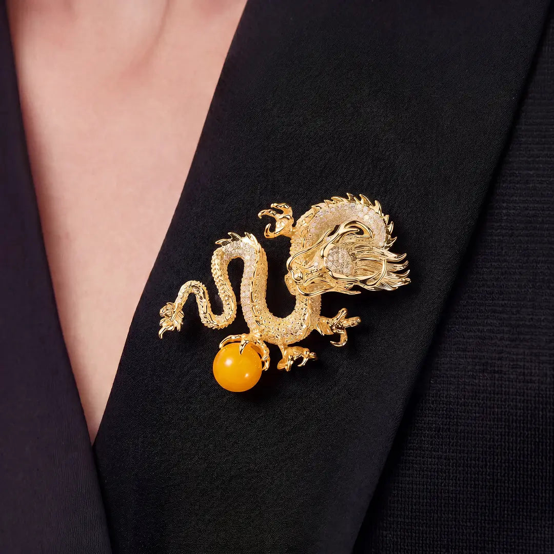 Aiko Tanaka Ryuko brooch, a gold dragon holding an amber orb, worn on a black V-neck top