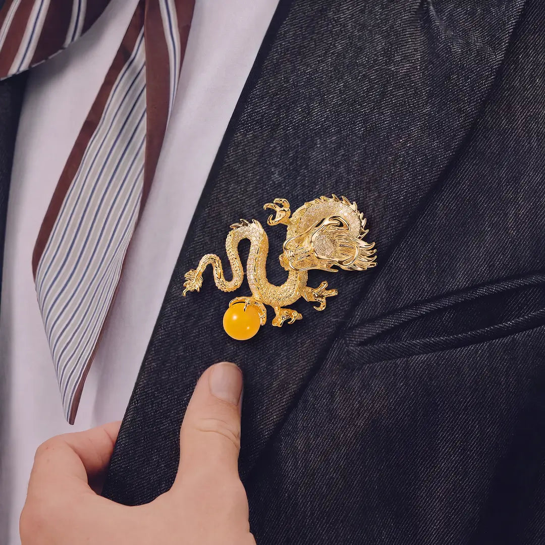 Aiko Tanaka Ryuko brooch, a gold dragon with an amber orb, pinned to a black blazer lapel worn with a striped tie