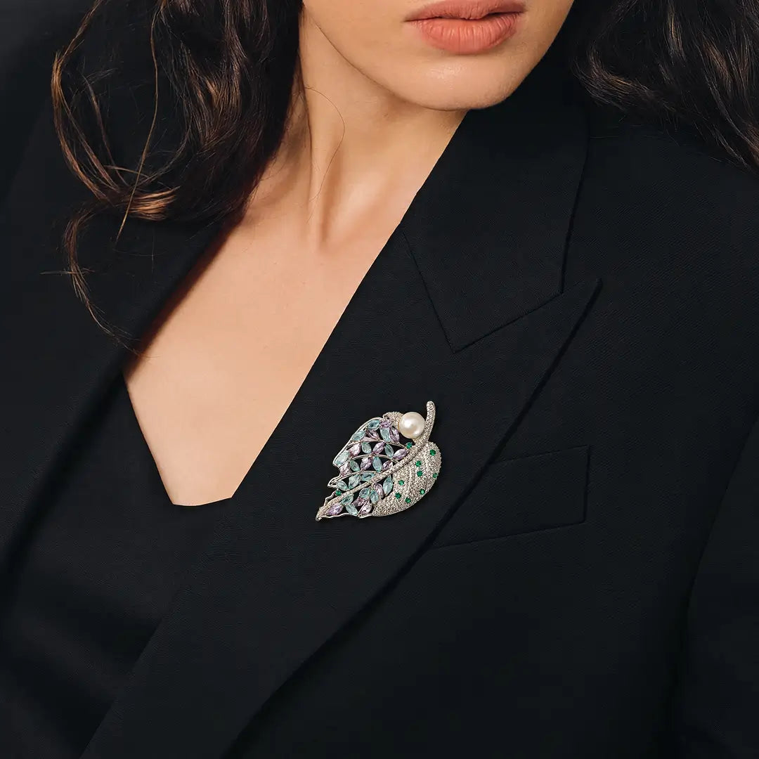 Aiko Tanaka Shion brooch, a silver crystal leaf with a pearl, pinned to a black blazer worn by a dark-haired model