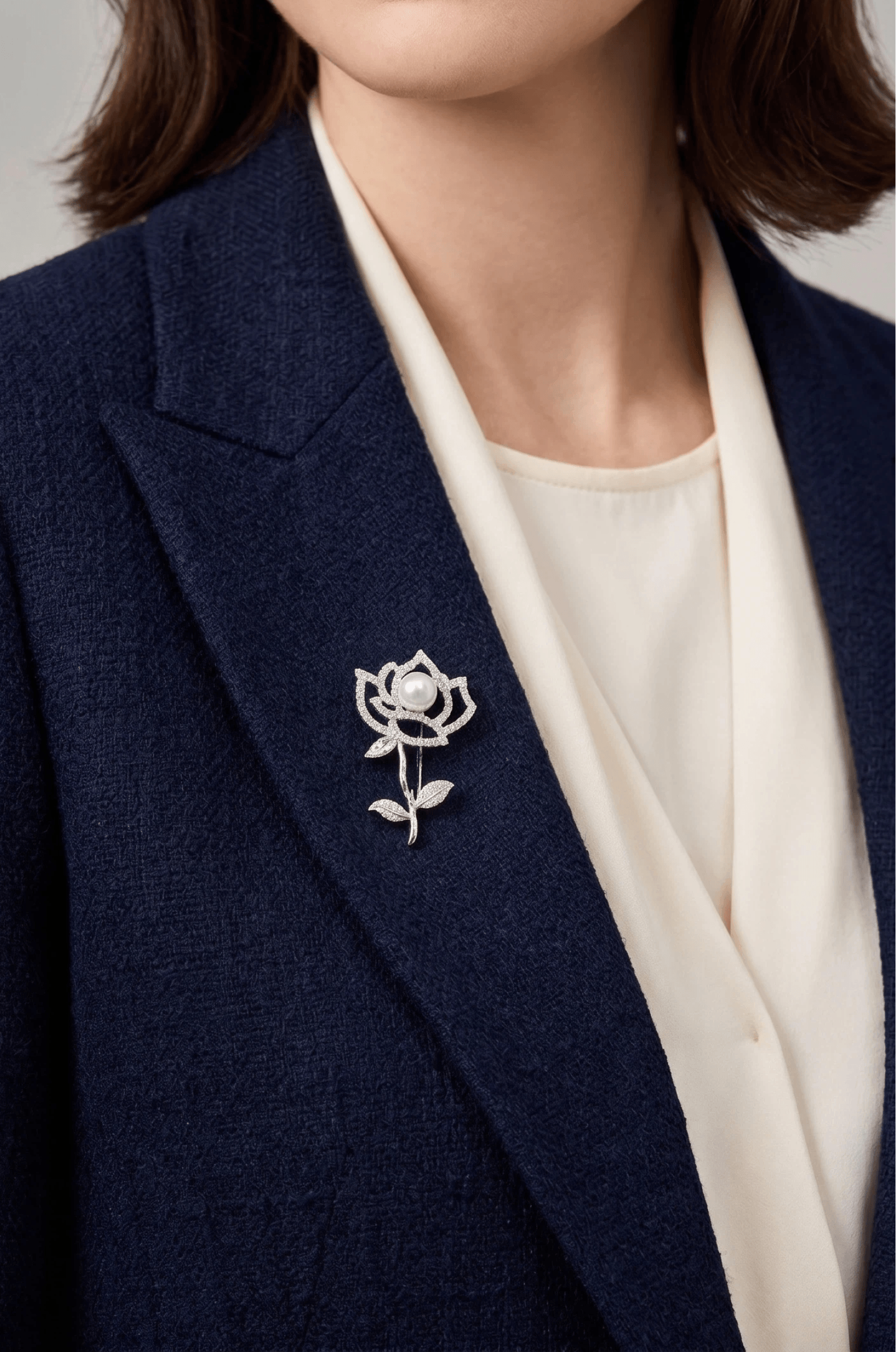 Woman in a navy tweed blazer over a cream blouse wearing the Aiko Tanaka Shiro Bara crystal rose and pearl brooch